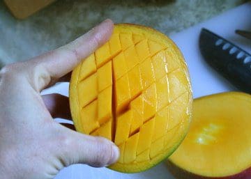 A person cutting a mango with a knife.