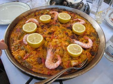 A plate of paella with shrimp and lemon wedges.
