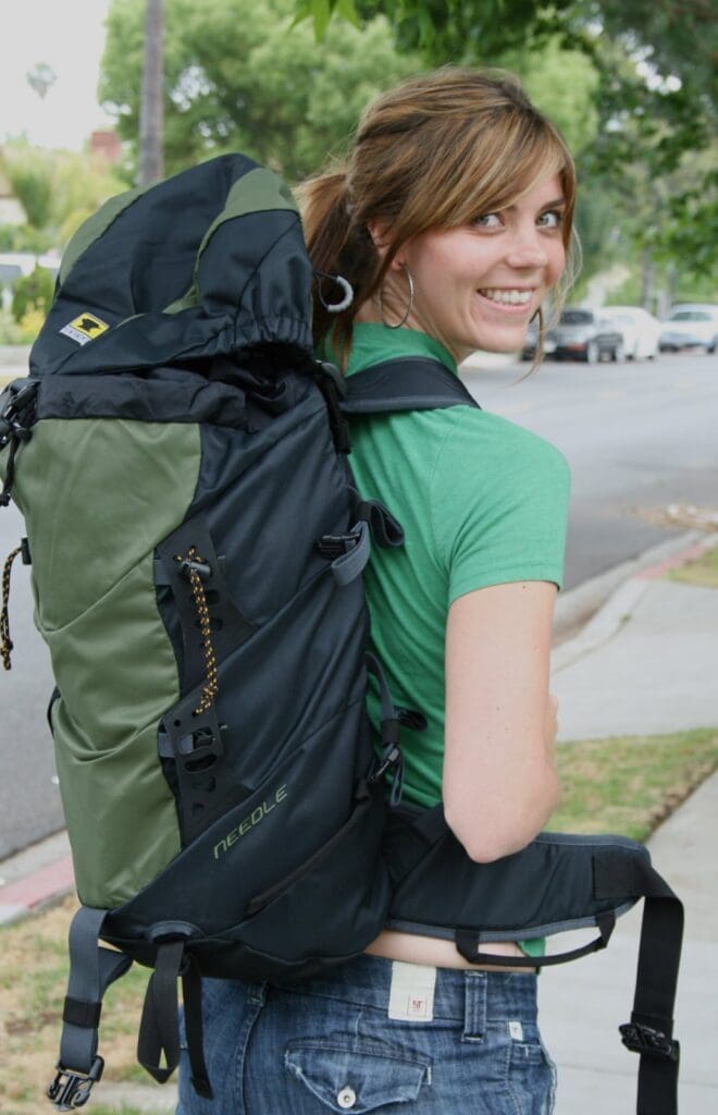 A woman standing on a sidewalk with a backpack.