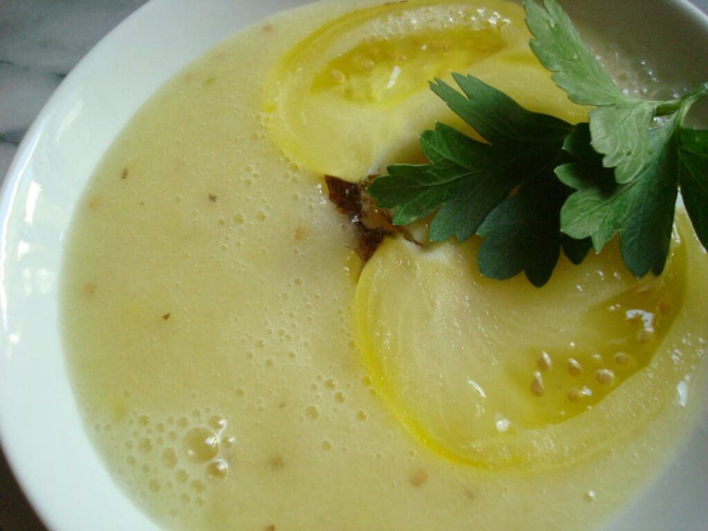 A bowl of soup with a slice of lemon and parsley.