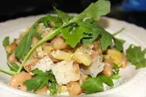 A white bean and arugula salad drizzled with parmesan on a plate.