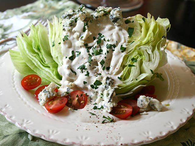A plate with lettuce, tomatoes and blue cheese dressing.