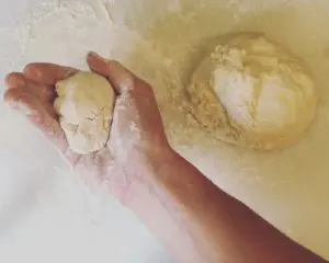 A person's hand is holding a ball of dough for a basic pizza recipe.
