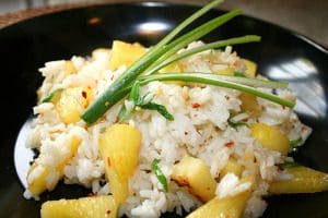 A black plate with rice and pineapple.