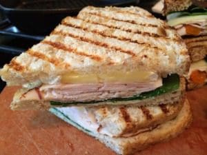 A grilled turkey sandwich with brie on a cutting board.