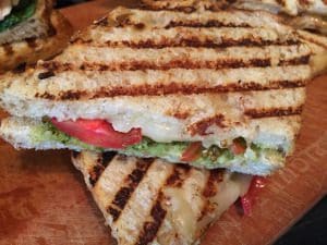 Two grilled sandwiches, one with tomato, on a wooden cutting board.