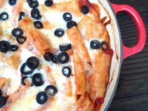 A dish of baked pasta with black olives and cheese in a red pan.