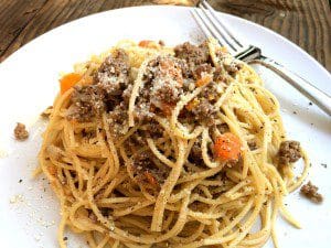 A plate of spaghetti with beef and vegetables on a wooden table, inspired by a bolognese recipe.