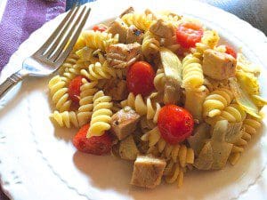 A plate of pasta with chicken and tomatoes on it.