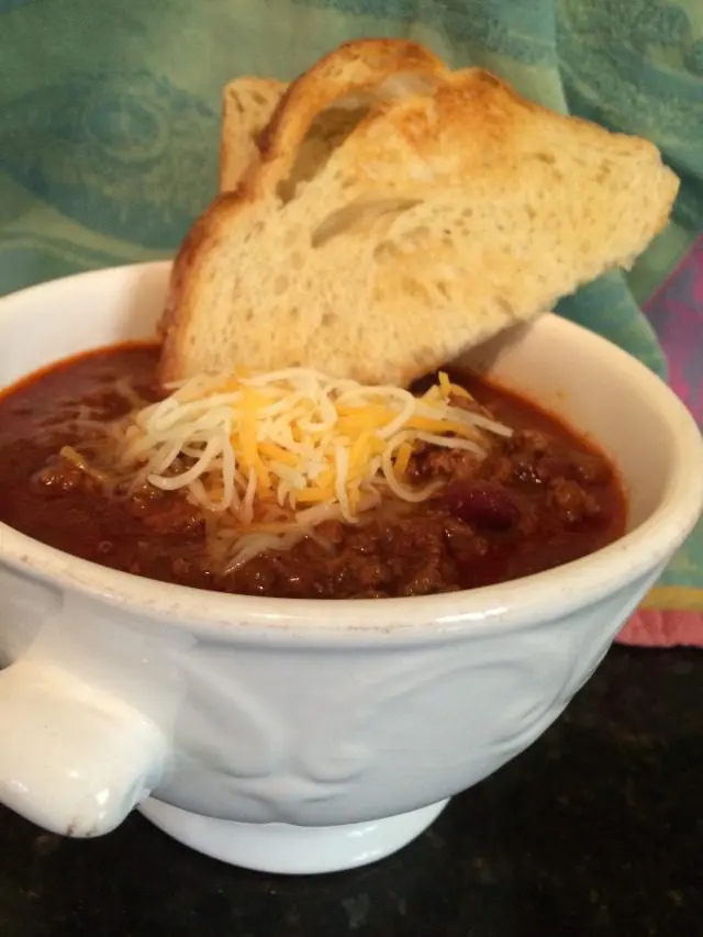 Chili in a bowl with bread and cheese.