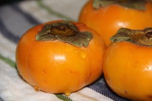 Three persimmons sitting on a towel.