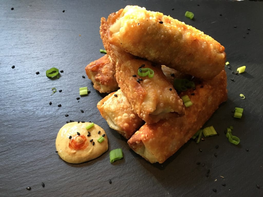 Fried spring rolls on a plate with sesame seeds.