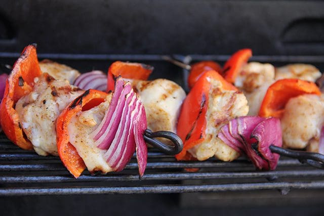 Chicken skewers with peppers and onions on a grill.