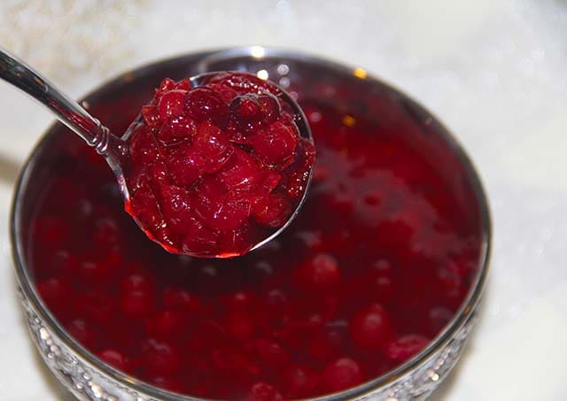 a ladle scooping out cranberry sauce from a bowl