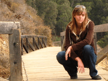 A woman squatting on a wooden bridge.