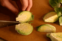 A person cutting brussels sprouts on a cutting board.