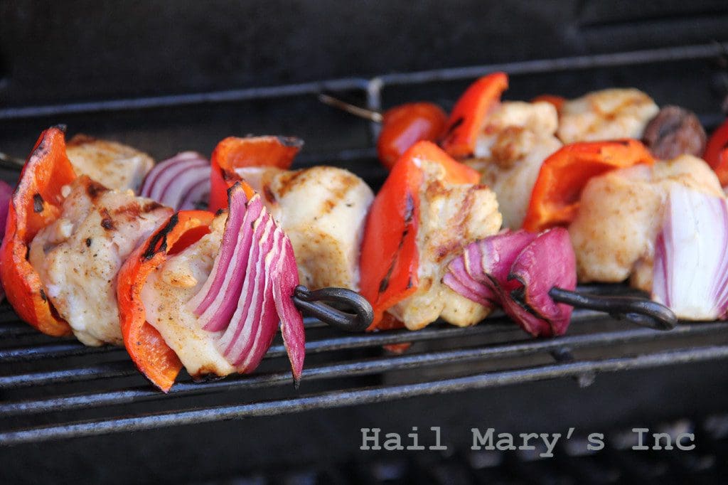Chicken skewers on a grill with peppers and onions.