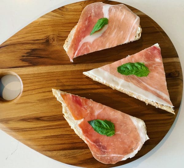 Three slices of prosciutto on a wooden cutting board.