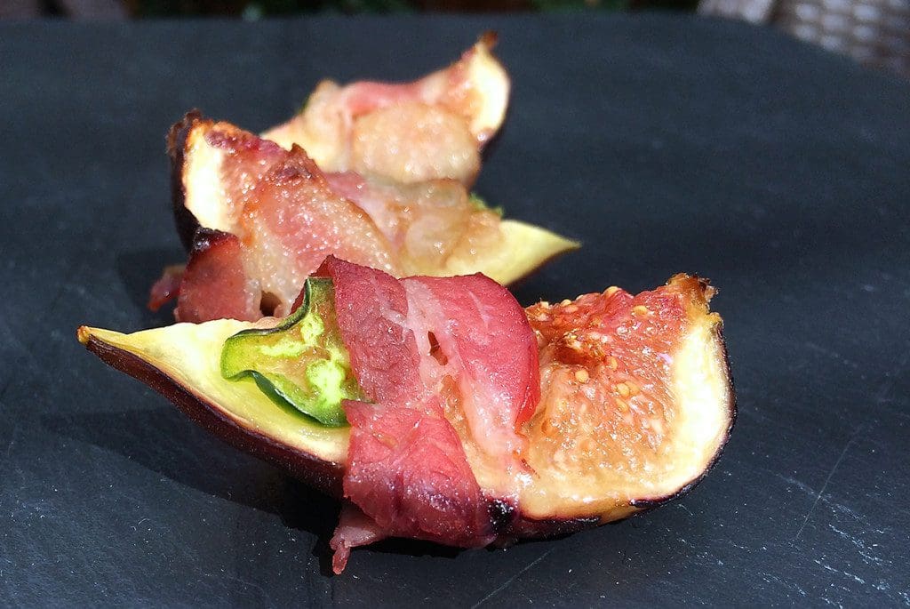 Figs wrapped in bacon on a black table.