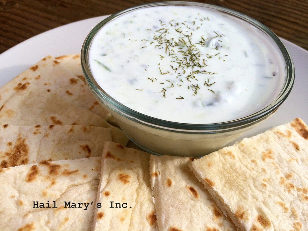 A bowl of dill dip with pita chips on a plate.