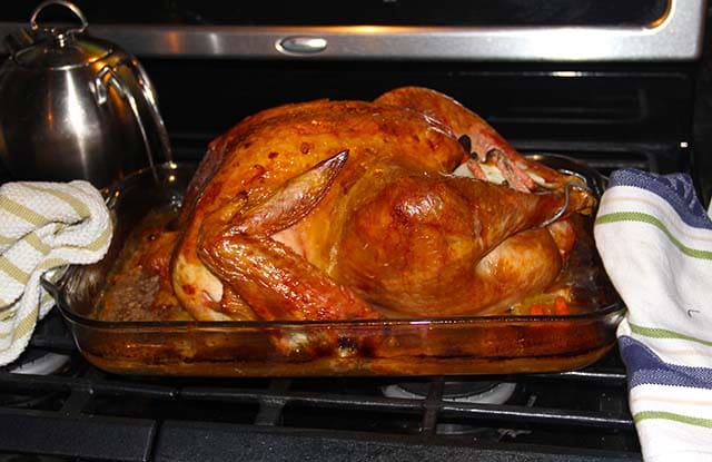 A turkey in a baking dish on top of an oven.