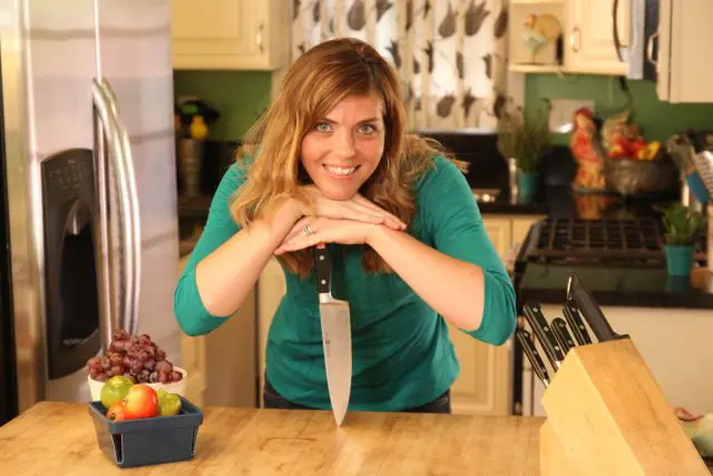 A woman posing in front of a kitchen counter with a knife.
