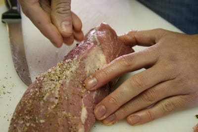 a pair of hands putting seasonings on a slice of raw meat