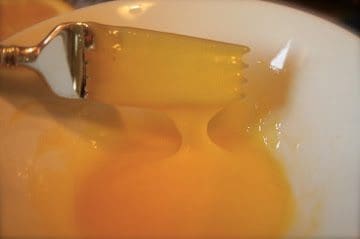 A spoon is being used to stir a bowl of orange juice.