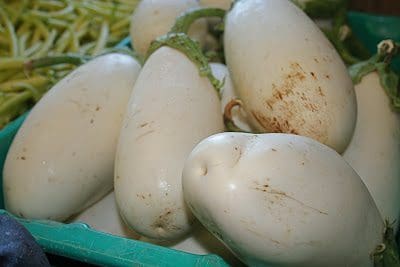 A bunch of white eggplants in a green crate.