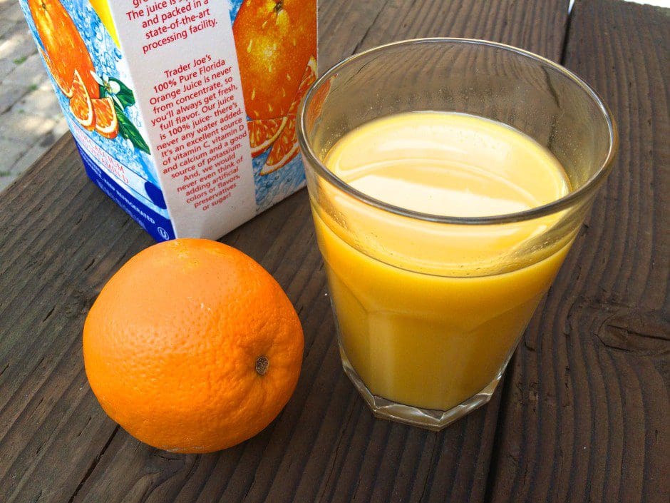 A glass of orange juice next to a carton of orange juice.