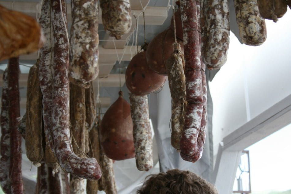 A woman looking at a bunch of sausages hanging from the ceiling.