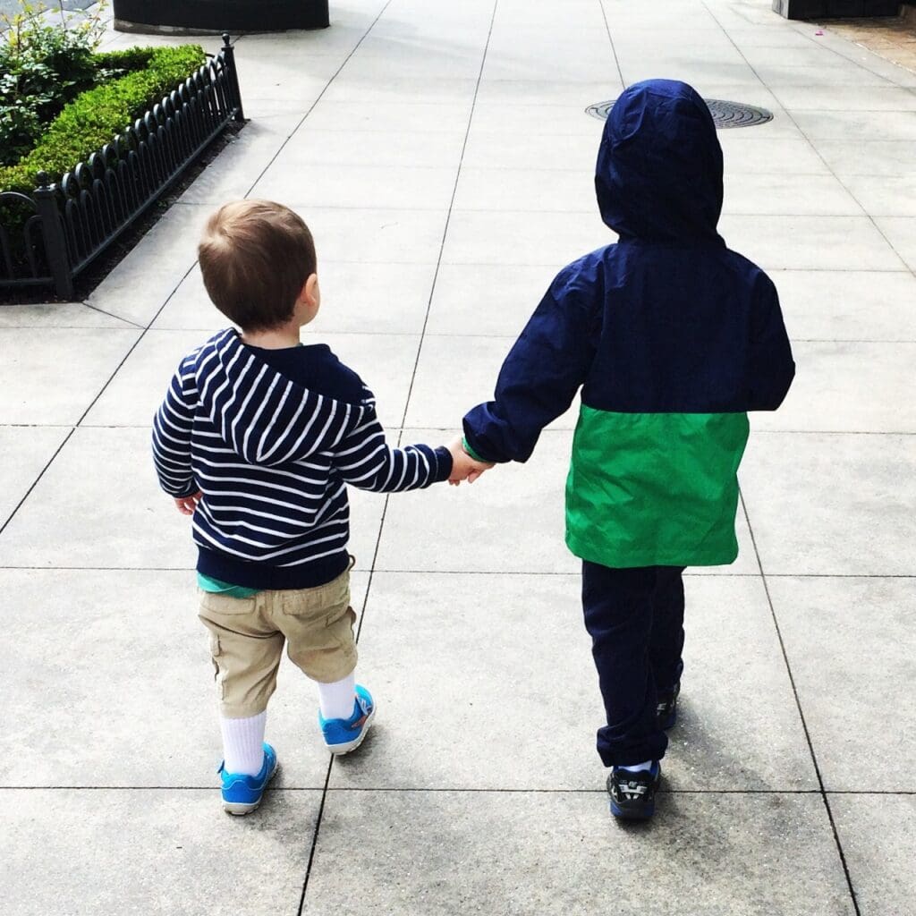 Two boys holding hands while walking down a sidewalk.