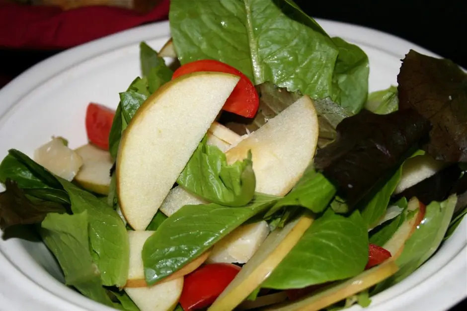 A white bowl of salad with apples and tomatoes.