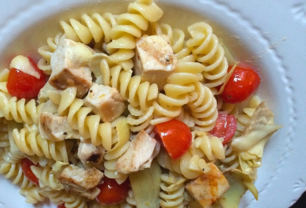 A plate of pasta with chicken, tomatoes and artichokes.