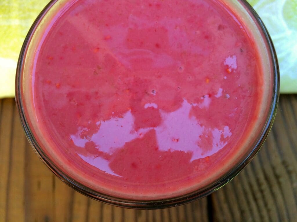 A pink smoothie in a glass on a wooden table.
