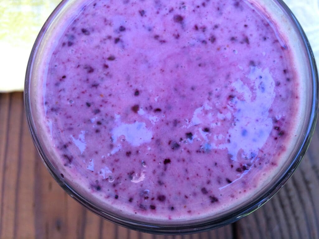 A blueberry smoothie in a glass on a wooden table.