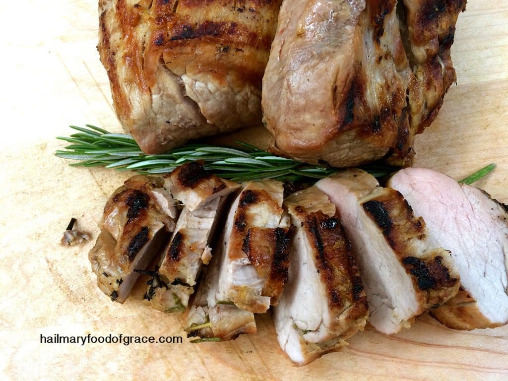 Grilled pork chops with rosemary sprigs on a cutting board.