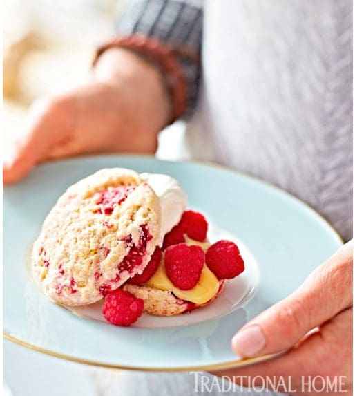 A person is holding a plate of raspberry scones.