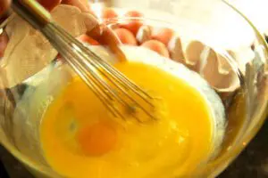 A person is whisking eggs in a glass bowl.