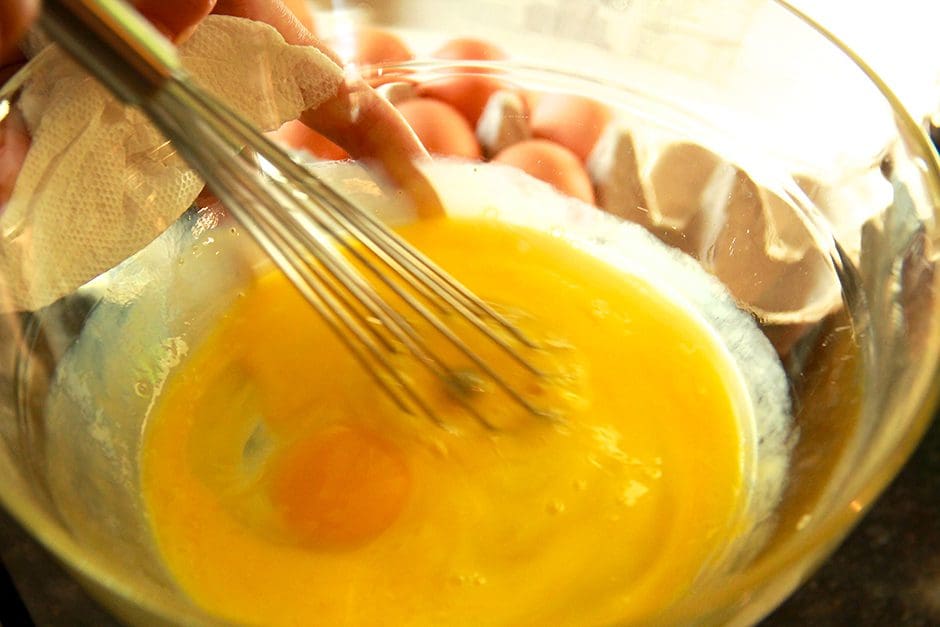 A person is whisking eggs in a glass bowl.