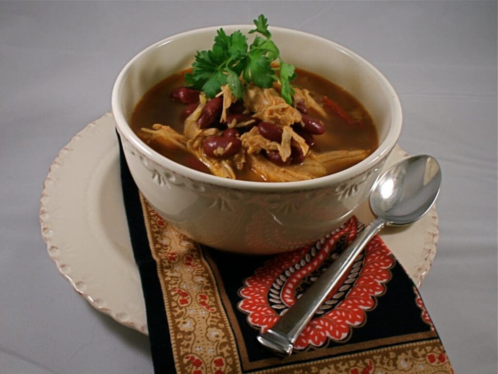 A bowl of soup with chicken and beans on a plate.