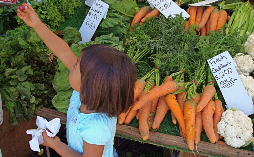 A little girl looking at vegetables at a farmers' market.