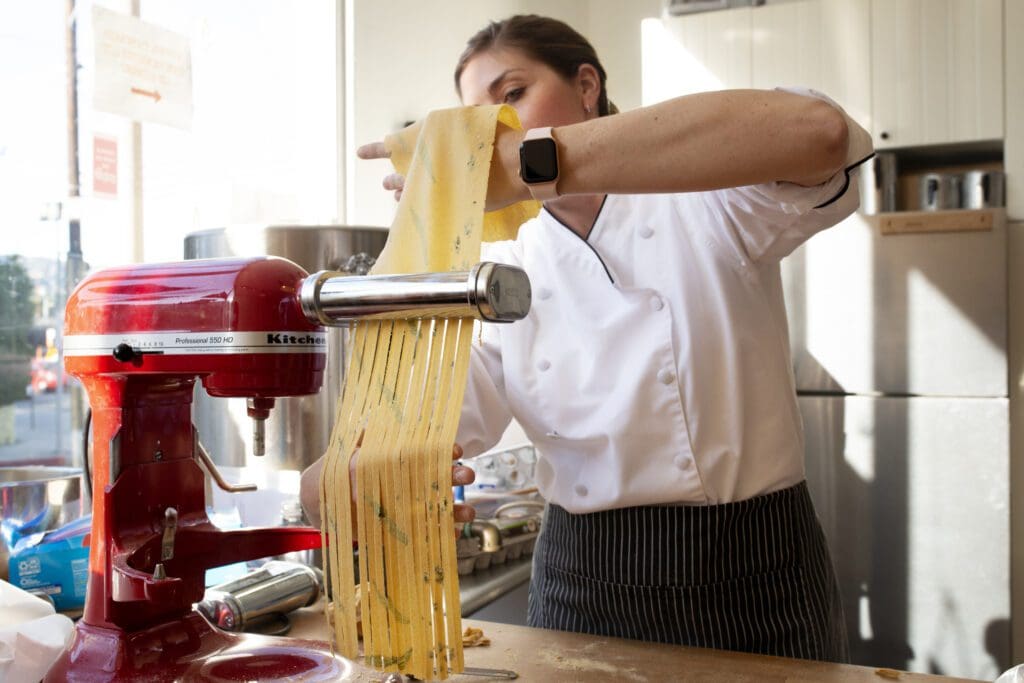 a woman making noodles from scratch using a machine