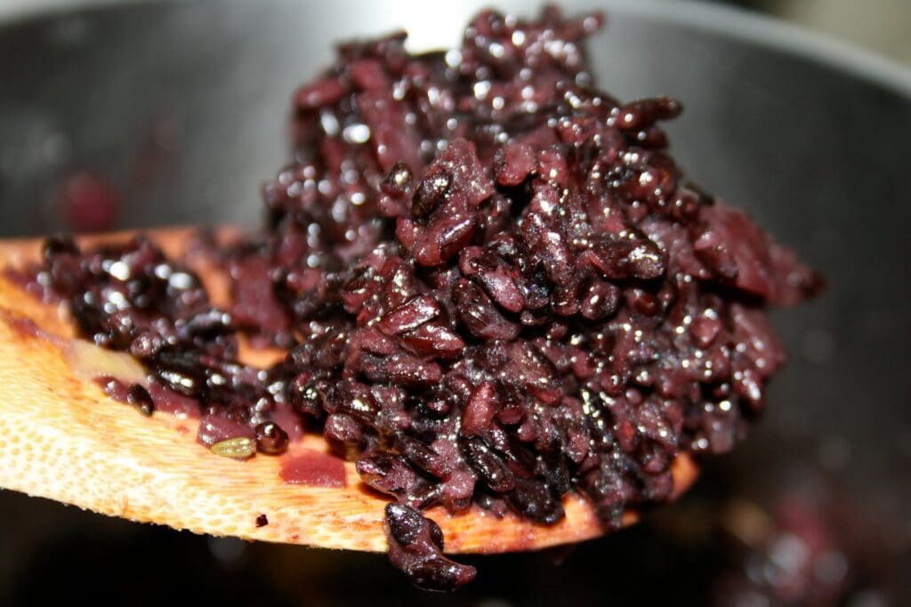 A wooden spoon full of black rice in a pot.