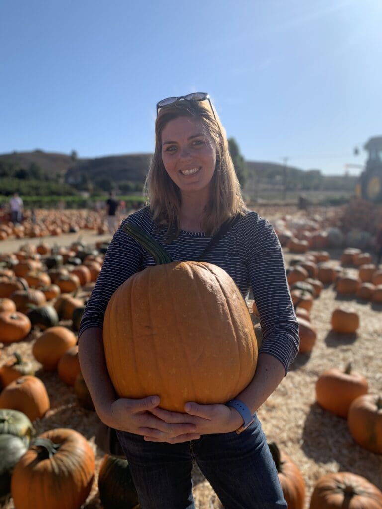 A woman holding a large pumpkin in a field.