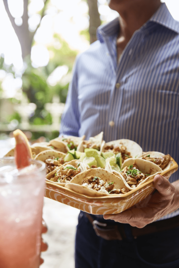 A man holding a tray of tacos and a drink.