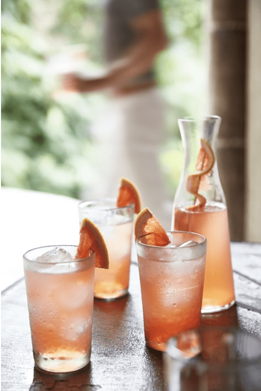 Three glasses of grapefruit infused gin and tonic on a wooden table.