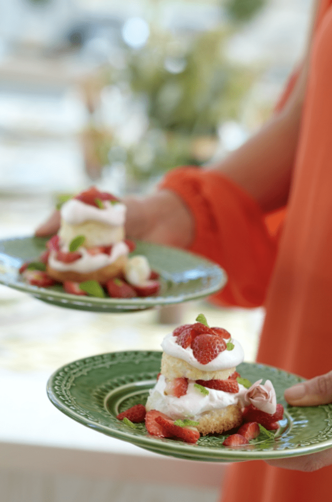 A woman is holding two plates of desserts with strawberries on them.