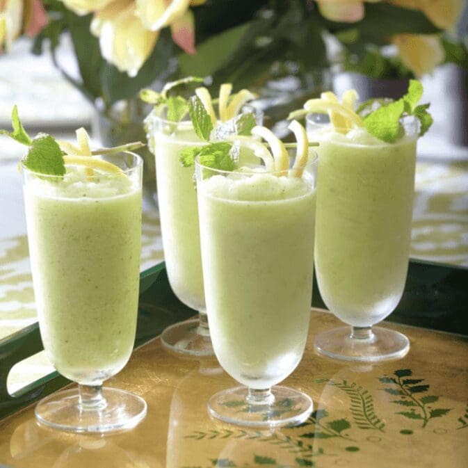 Four glasses of lemonade with mint leaves on a tray.