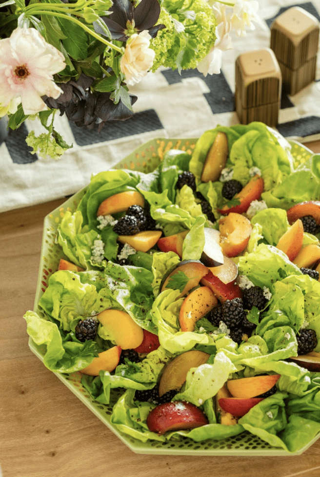 A salad with peaches and blackberries on a wooden table.